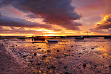Obraz premium Sunset over beached fishing boats in Morecambe Bay, Lancashire, England. The estuary of Morecambe Bay is the largest area of intertidal mudflats and sand in the United Kingdom