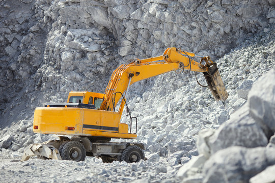 Hydraulic hammer crushes large stones in a stone quarry, closeup. Heavy mining equipment.