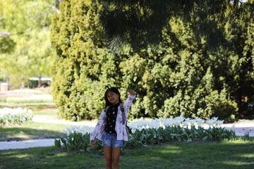 An asian girl poses happy in front of trees and white tulips