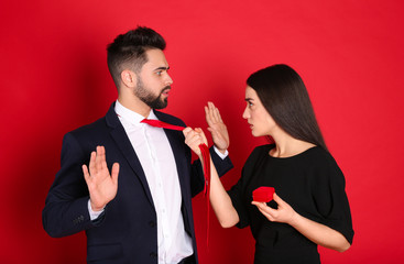 Young woman with engagement ring making marriage proposal to her boyfriend on red background