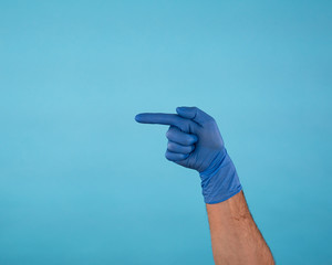 Male Hand in blue surgical latex gloves pointing to the left isolated on blue background