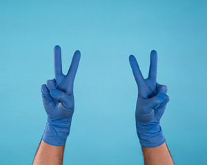 Male Hands in blue surgical latex gloves making peace signs isolated on blue background