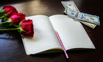 A few red roses and dollars are on the table next to the Notepad