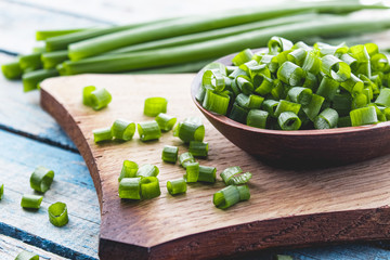 Fresh green onion chopped and lies on a bowl on a chopping board on a background of blue boards.