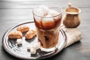 Glass of tasty iced coffee with cookies on table