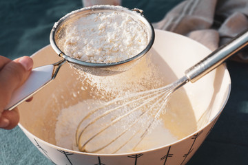 Detail of a woman hands sifting flour with a strainer on a bowl. Cooking and ingredients.