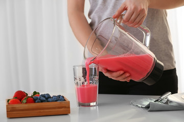 Woman pouring healthy smoothie into glass in kitchen