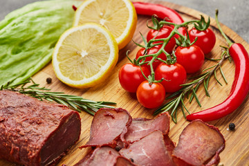 Armenian basturma or Pastirma on wooden cutting board decorated with spices, lettuce, lemon and tomatoes. Meat smoked jerky good as Beer snack
