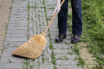 Women cleaning cut grass from pavement using classic broom made from natural materials