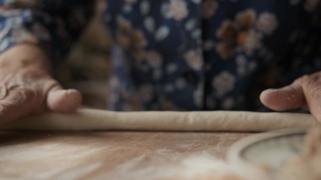 An elderly woman rolls the dough on the table. Only hands in frame