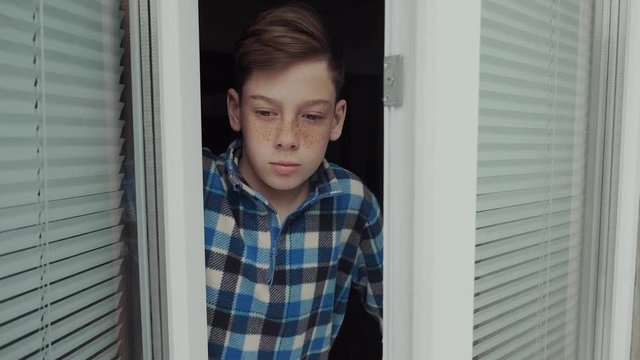 A 13-year-old teenager is deprived of a walk in the fresh air due to forced quarantine measures in connection with the COVID-19 pandemic. He looks out with regret and sadness from the window of his