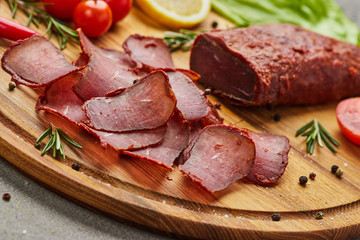 Armenian basturma or Pastirma on wooden cutting board decorated with spices, lettuce, lemon and tomatoes. Meat smoked jerky good as Beer snack