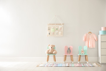 Cute toys on chairs with bunny ears near white wall indoors, space for text. Children's room...