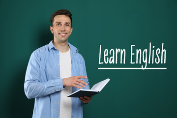 Young English teacher with book near chalkboard