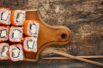 Sushi roll with salmon, avocado and cheese on wooden board on rustic background. Japanese restaurant menu