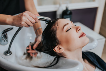 Professional hairdresser washing hair of a beautiful young  woman in hair salon. .