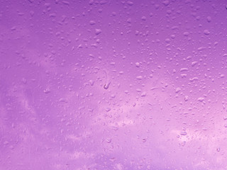 Wet pink window with rain drops and a cloudy sky outside.