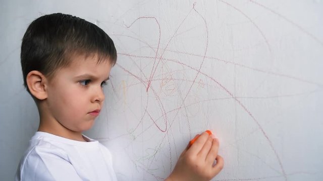The child draws on the wall with colored chalk. The boy is engaged in creativity at home