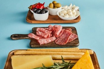 Selective focus of antipasto ingredients on boards on blue background