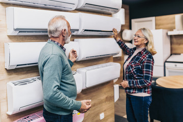 Senior husband and wife, satisfied customers choosing air conditioner in appliances store.