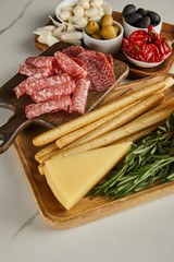 High angle view of boards with salami slices, breadsticks, cheese and antipasto ingredients on white background