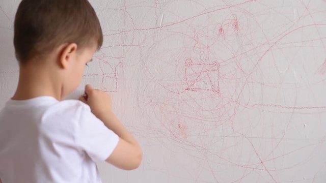 Boy draws on the wall with colored chalk. The child is engaged in creativity at home