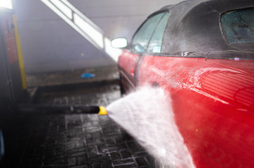 washing a red car convertible manually by brush with foam.