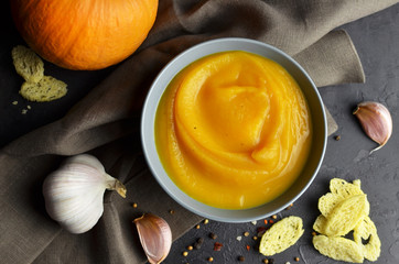 Pumpkin soup in a bowl with fresh pumpkin, garlic, croutons and spices on rustic background....