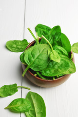 Spinach leaves in wooden bowl over white wooden table background. Vegan food trend. Green living concept.