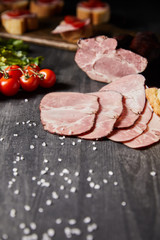 selective focus of tasty ham sliced ham, cherry tomatoes, parsley, salt on wooden grey table