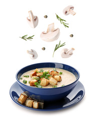 Fresh mushrooms, rosemary and peppercorns falling into bowl with homemade soup on white background