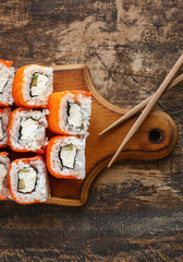 Sushi set with Philadelphia cheese, avocado and salmon on a brown wooden board.