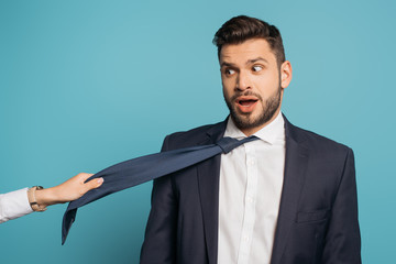 partial view of woman pulling tie of surprised businessman on blue background