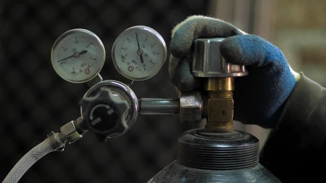 In the workshop. Close-up. The man opens an oxygen cylinder for welding
