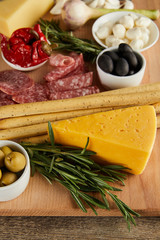 Selective focus of board with cheese, breadsticks, salami slices and antipasto ingredients on wooden background