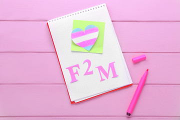Notebook with paper heart and abbreviation F2M on color wooden background. Concept of transgender