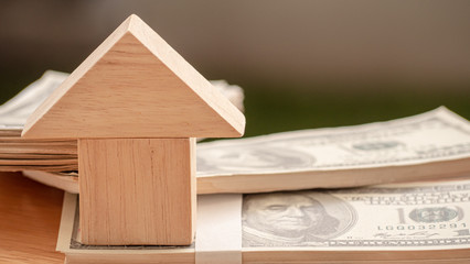 The model of a wooden house is stacked near the money dollar.  Concept Having a house or buying a home or home loan.