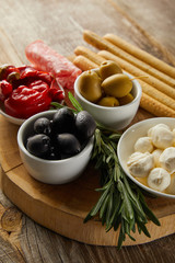 Selective focus of breadsticks, salami slices and rosemary near bowls with antipasto ingredients on board on wooden background