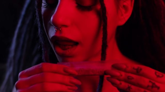 close-up girl tongue licking paper with marijuana for further drug use. paper ganja, legalization of marijuana