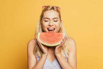beautiful, blonde girl with closed eyes eating juicy watermelon on yellow background