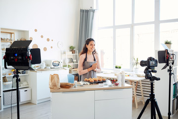 Professional baker standing alone in kitchen recording cupcakes cooking process video on camera for her vlog channel