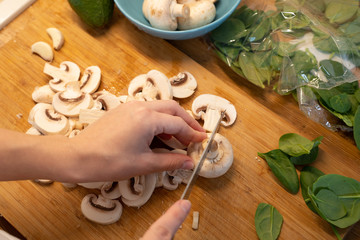 Woman cutting mushroom on table, close-up. Hands cutting mushrooms on a cutting board. Young woman cutting mushrooms in the kitchen.