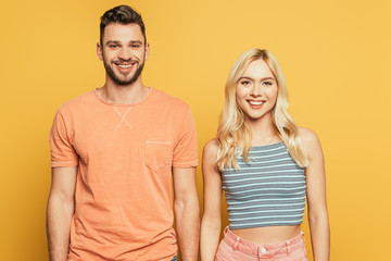 happy handsome man and attractive blonde girl smiling at camera isolated on yellow