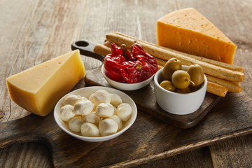 High angle view of bowls with olives, cheese, mozzarella and marinated chili peppers on boards on wooden background