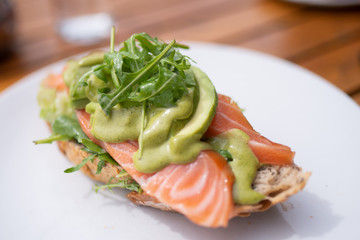 
Fetta di pane con fette di salmone, crema di avocado e rucola servita su un piatto
