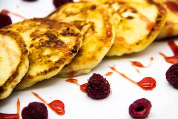 Ukrainian cottage cheese fritters, syrniki with jam on white plate. Cheese pancakes with raspberry without GMO. Delicious breakfast food at the morning.