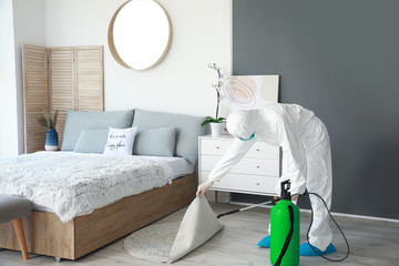 Worker in biohazard suit disinfecting house