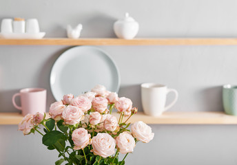Utensils, bouquet of roses and mugs on shelf. Dishes in cupboard in kitchen.