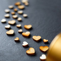 Love concept. Little wooden hearts falling out of a small gold gift box on a dark background.