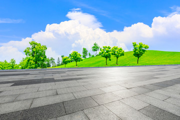 Empty square ground and green grass with tree under blue sky.